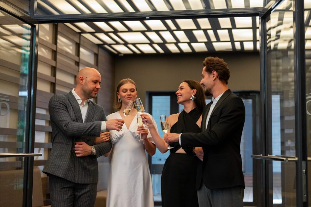 Four well-dressed adults clinking champagne glasses in a modern office setting, celebrating success, partnership, and financial security.