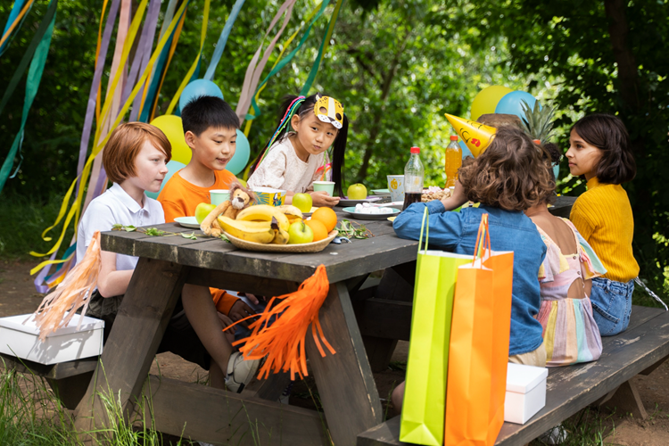 Event insurance – children enjoying a colorful outdoor party with decorations, gifts, and picnic seating.